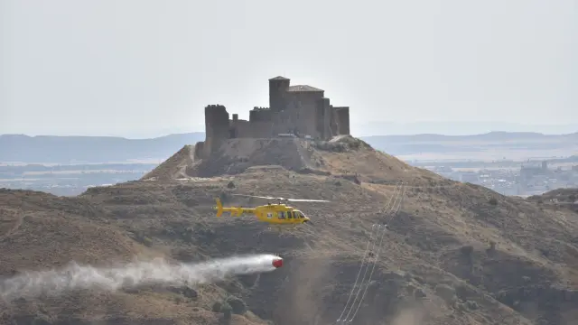 Un helicóptero de extinción cruza por delante del castillo de Montearagón, próximo a la zona del incendio.
