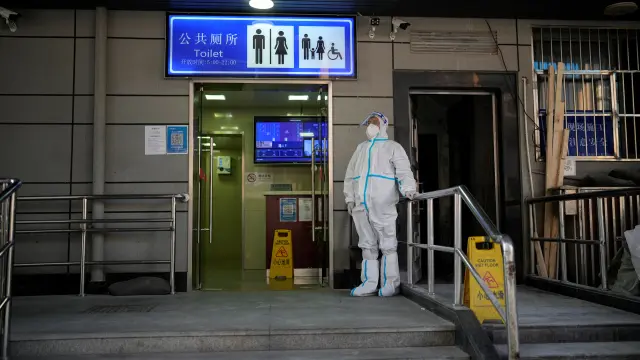 A worker in protective suit keeps a watch outside a public toilet in Shanghai
