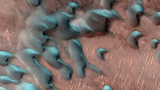 Esta imagen adquirida el 22 de julio de 2022 por el Mars Reconnaissance Orbiter de la NASA muestra dunas de arena moviéndose por el paisaje. La escarcha invernal cubre la mitad más fría de cada duna que mira al norte