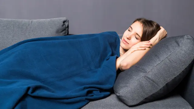 Pretty girl sleeping on a sofa covered with blue coverlet on gray background