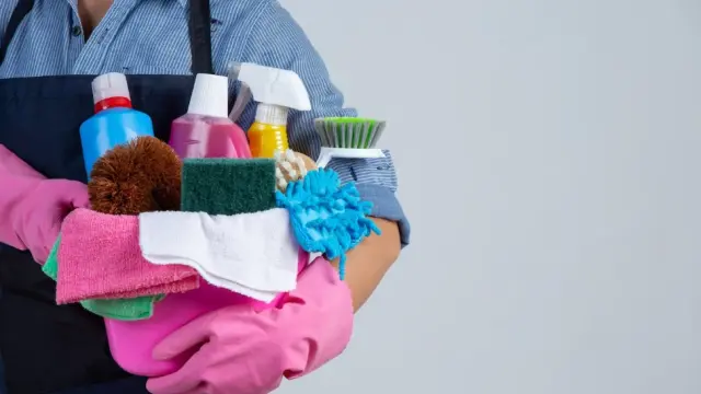 Una empleada del hogar sostiene un cubo con productos de limpieza