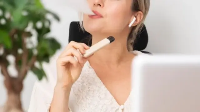Una persona fumando de un cigarrillo electrónico frente a la pantalla de un ordenador