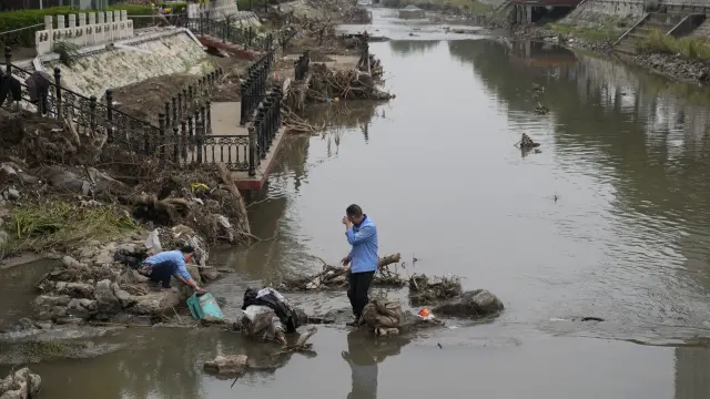 Residents wash their suitcase and belongings on a damaged bank of a canal clogged with flood debris in the aftermath of flood waters from an overflowing river in the Mentougou district on the outskirts of Beijing on Monday, Aug. 7, 2023. The death toll in recent flooding in China's capital rose, officials said Wednesday, as much of the country's north remains threatened by unusually heavy rainfall. (AP Photo/Andy Wong)