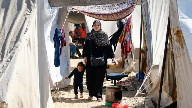 A woman walks with a child as displaced Palestinians, who fled their houses amid Israeli strikes, take shelter at a tent camp at a United Nations-run centre, in Khan Younis in the southern Gaza Strip, October 30, 2023. REUTERS/Ibraheem Abu Mustafa