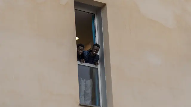 Dos de los migrantes que se alojan en el albergue de Cella se muestran sonrientes desde una de las ventanas