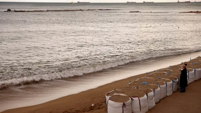 Un turista bebe junto a bolsas llenas de arena para proteger la terraza de un 'Chiringuito' en la playa de la Barceloneta.
