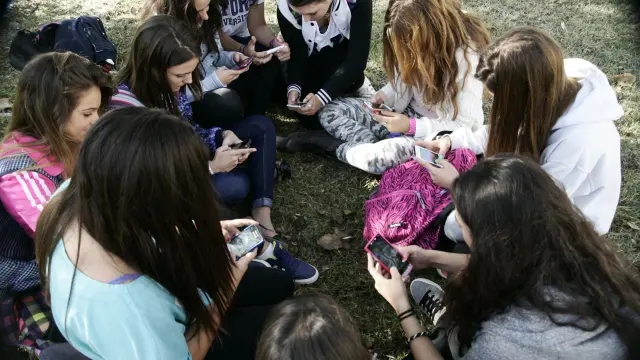 Adolescentes arremolinados en torno a sus móviles durante una pausa lectiva.