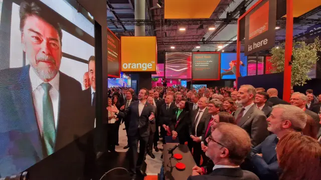 Autoridades y asistentes en un evento tecnológico de Orange frente a una pantalla grande mostrando a un orador.