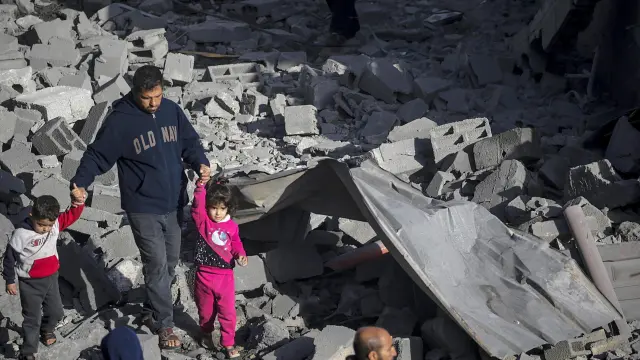 Un palestino con dos niños camina entre los escombros de una casa destruida tras los ataques aéreos israelíes en el campo de refugiados de Al Nusairat, Franja de Gaza