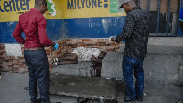 ATENCIÓN EDITORES: CONTENIDO GRÁFICO EXPLÍCITO - AME9715. PUERTO PRÍNCIPE (HAITÍ), 18/03/2024.- Dos hombres se disponen a levantar el cadáver de una mujer en el suelo este lunes, en Puerto Príncipe (Haití). Doce cadáveres fueron encontrados este lunes en Petion-Ville, en las colinas de Puerto Príncipe, en circunstancias aún por aclarar, como la identidad de las víctimas, que no se descarta sean miembros de bandas armadas abatidos por la Policía Nacional. Los cuerpos, entre ellos el de una mujer, fueron hallados dispersos en plena vía, en los alrededores de una zona dedicada al comercio informal de alimentos y otros productos. EFE/ Johnson Sabin