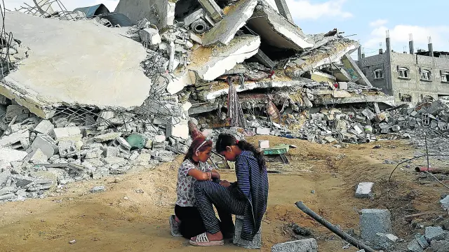 Dos niñas permanecen sentadas junto a su casa destruida por las fuerzas israelíes en Rafah.