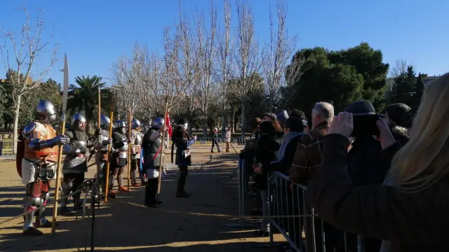 Un soldado explica las armaduras usadas en la práctica de esgrima medieval, rodeado de visitantes que prestan atención a su relato.