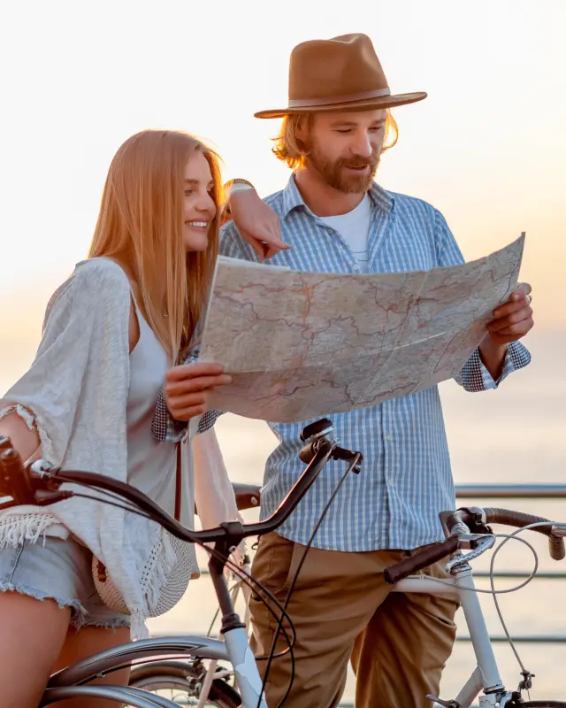 attractive happy couple traveling in summer on bicycles, man and woman with blond hair boho hipster style fashion having fun together, looking in map sightseeing