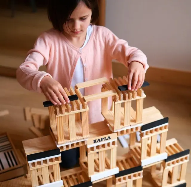 Una niña hace una construcción con el juego educativo Kapla, de madera natural y sostenible, que vende Guiro Juguetería.
