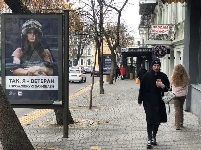 Una mujer pasea ante un cartel de una joven militar y armada
