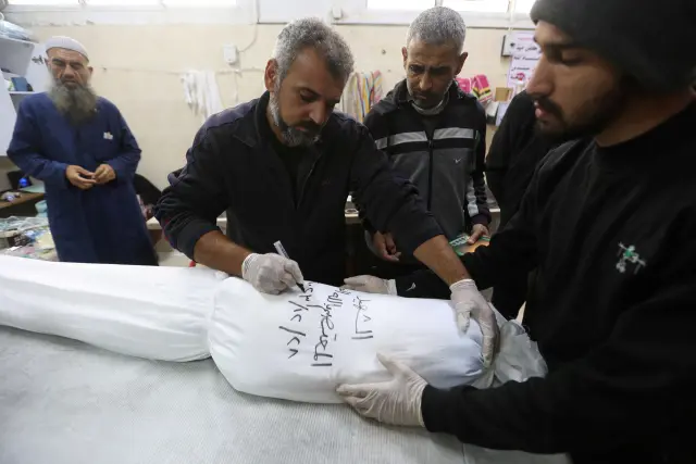 Mohammed Abu Mussa, voluntario de la sociedad Keratan que prepara cadáveres para el entierro, escribe el nombre y la fecha en un sudario blanco que cubre el cuerpo de un palestino muerto en un ataque israelí