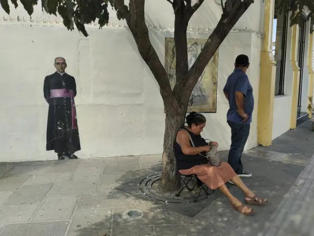 Una pareja de salvadoreños se protege del sol ante una imagen del arzobispo Oscar Arnulfo Romero, San Romero de América, asesinado en marzo de 1980 / 02-02-2024 / Foto Gervasio Sanchez [[[FOTOGRAFOS]]]