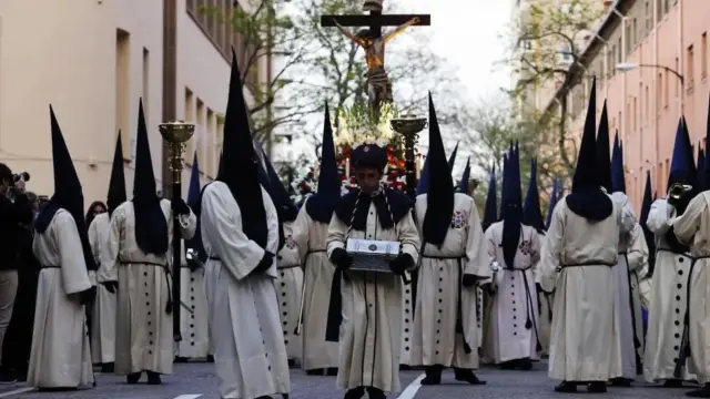 Hermanos de la Piedad con sus capirotes y un niño con bonete durante la procesión de Semana Santa de Zaragoza