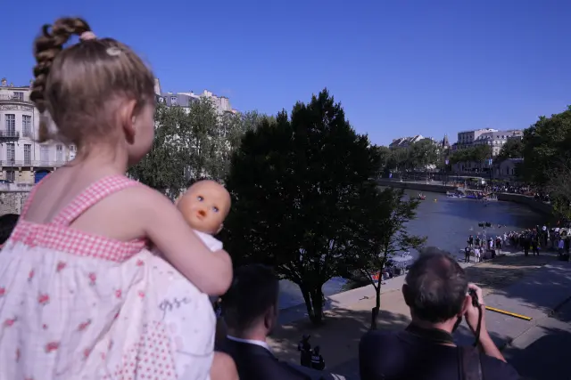 Laurine, 3, holds a doll on her father Nicholas' shoulders as she watches Paris Mayor Anne Hidalgo swimming in the Seine river, Wednesday, July 17, 2024, in Paris, France. After months of anticipation, Anne Hidalgo swam in the Seine River Wednesday, fulfilling a promise she made in January nine days before the opening ceremony of the 2024 Olympics. (AP Photo/David Goldman)