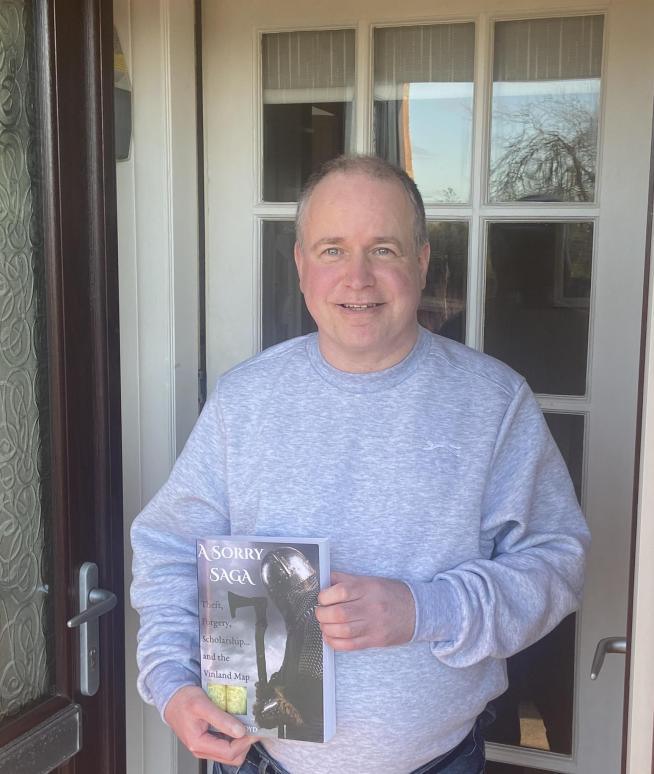 John Paul Floyd, a la puerta de su casa y con un ejemplar de su libro en las manos.