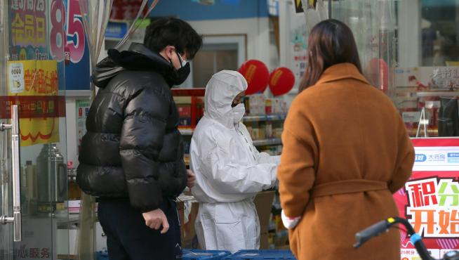 El dependiente de una farmacia de Wuhan a los clientes con un traje de protección por el coronavirus