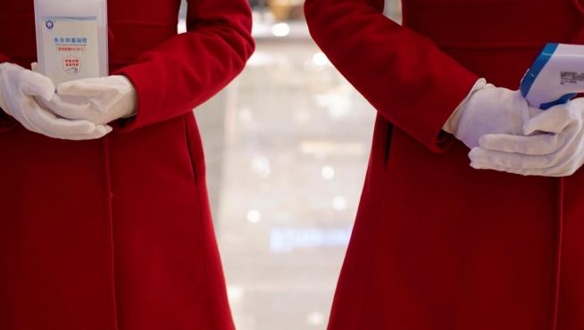 Dos empleadas de un centro comercial de Wuhan esperan a clientes con gel desinfectante y un termómetro.
