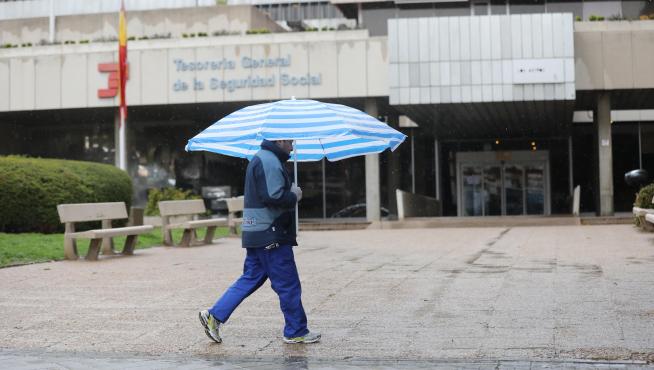 Un hombre con un paraguas pasa frente a una oficina de la Tesorería General de la Seguridad Social en Madrid.