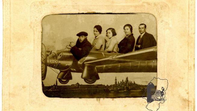 Tres mujeres y dos hombres dentro de un aeroplano pintado en un telón con vista de Zaragoza