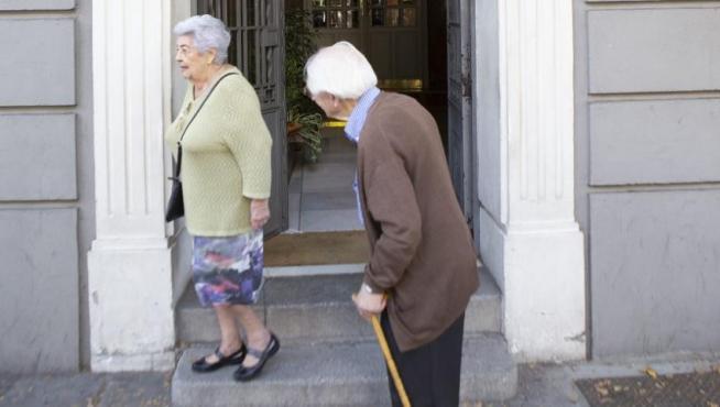 Dos personas mayores, delante de un portal donde se venden pisos.