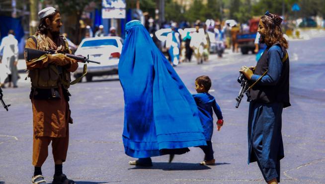 Una mujer con burka pasa junto a centinelas armados en una calle de Kabul.