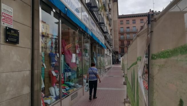 Una mujer pasa junto a Comercial Algodonera en una vallada calle del Teniente Coronel Valenzuela, afectada por las obras en la plaza de Salamero de Zaragoza