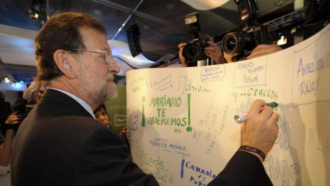 Rajoy escribe en un panel colocado en la sala donde se celebra la convención nacional del PP.