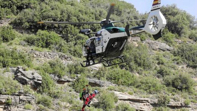 El helicóptero traslada con la grúa a un herido (de rojo) que va acompañado de un agente.