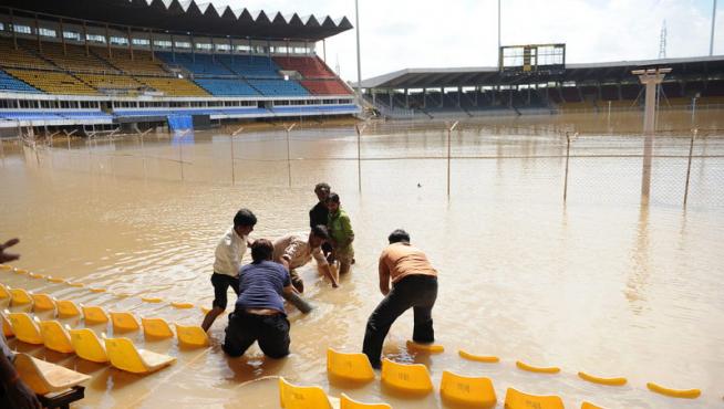Operarios indios intentan achicar agua en un estadio de críquet.