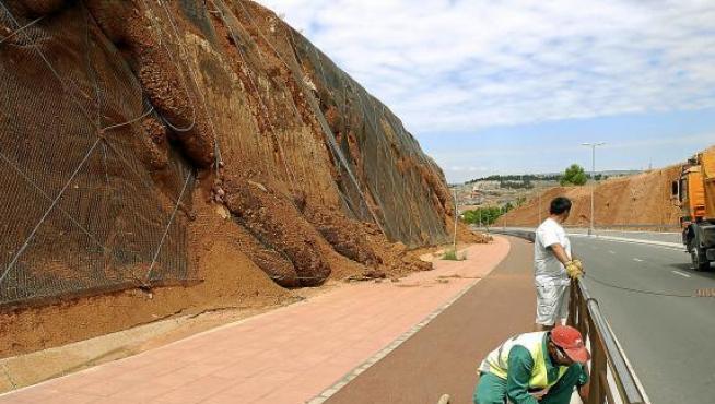 Operarios de Acciona preparan la intervención en la ladera que sufre derrumbamientos -a la izquierda-.