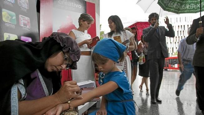 La venezolana Carol Ceva realiza un tatuaje de henna con palabras celtibéricas a María Cebrián, ayer en plena lluvia en Zaragoza.