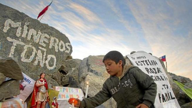 Un niño enciende una vela en un altar del campamento de la mina San José (Chile), ayer.