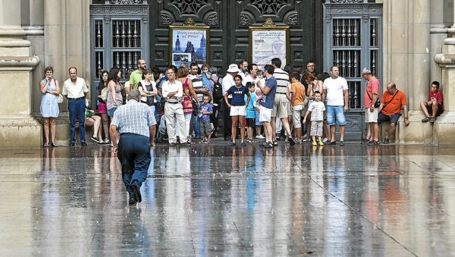 Paseantes y turistas se refugian de una tormenta en la entrada a la basílica del Pilar.