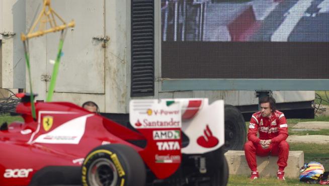 - El piloto español Fernando Alonso, de la escudería Ferrari, observa sentado fuera de pista cómo una grúa retira su monoplaza