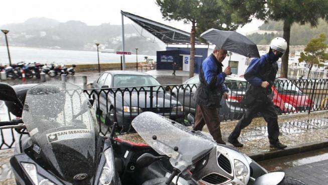 Dos conductores observan unos vehiculos derribados por el temporal en San Sebastián