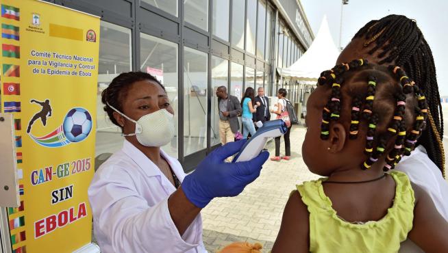 Una trabajadora sanitaria comprueba la temperatura de una niña pequeña en el aeropuerto de Bata (Guinea).