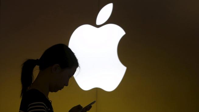 Una mujer mira la pantalla de su móvil frente a un logo de Apple