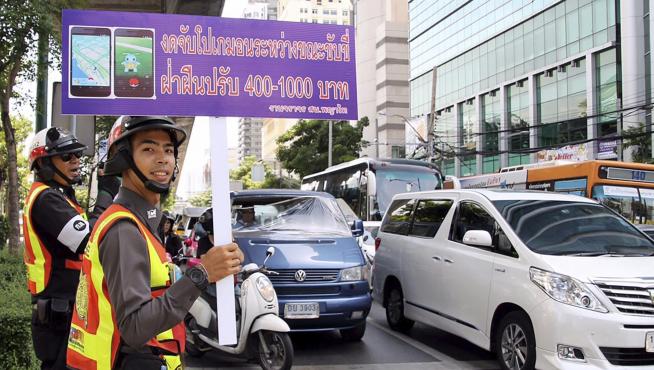 Un agente sostiene un cartel en el que se recuerda que está multado jugar mientras se conduce.