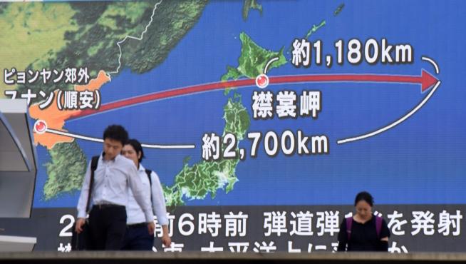 Varios viandantes en Tokio pasan delante de una pantalla que muestra la trayectoria del misil.