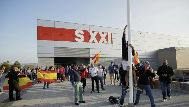 Varias personas han izado la bandera española a las puertas del pabellón siglo XXI.