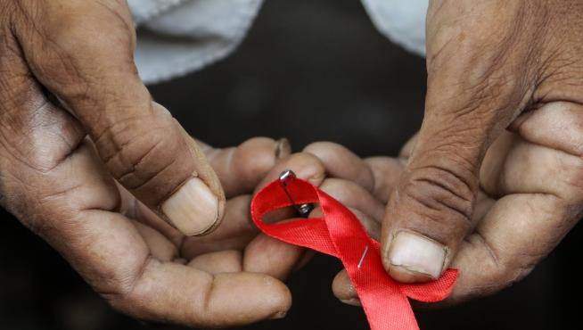 Un hombre sujeta un lazo rojo, símbolo de la lucha contra el sida.