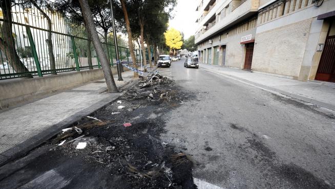 Restos del contenedor y el vehículo quemado en la calle de San Eugenio en Torrero.