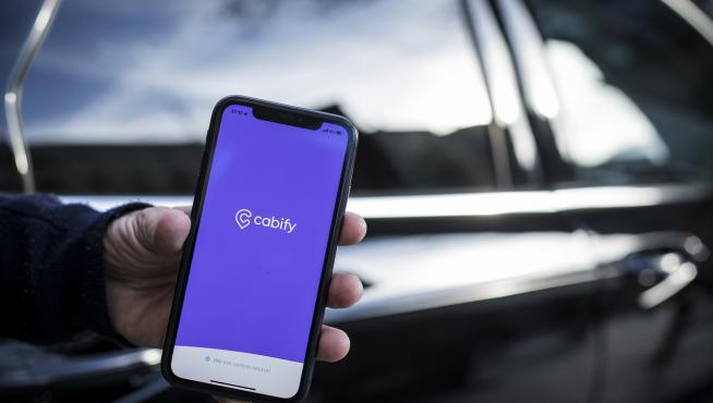 Un móvil con la aplicación de Cabify junto a uno de los coches que comenzarán a circular este miércoles en Zaragoza.