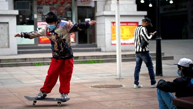 Un joven con mascarilla juega con un monopatín en Wuhan.