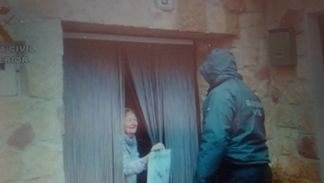 Un guardia entrega un paquete de medicinas a una pareja de mayores en un pueblo.